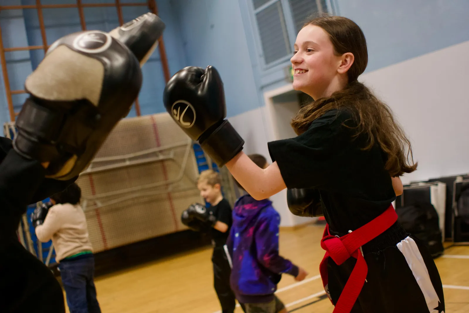 A girl in a red belt smiling as she punches a pad