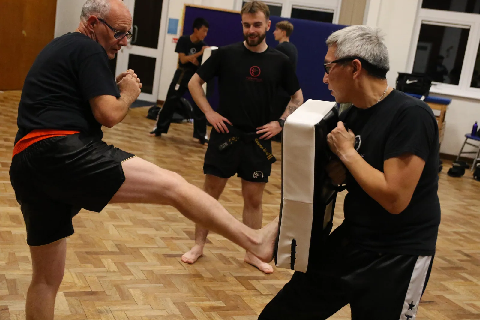 An older member kicking a pad held by his training partner