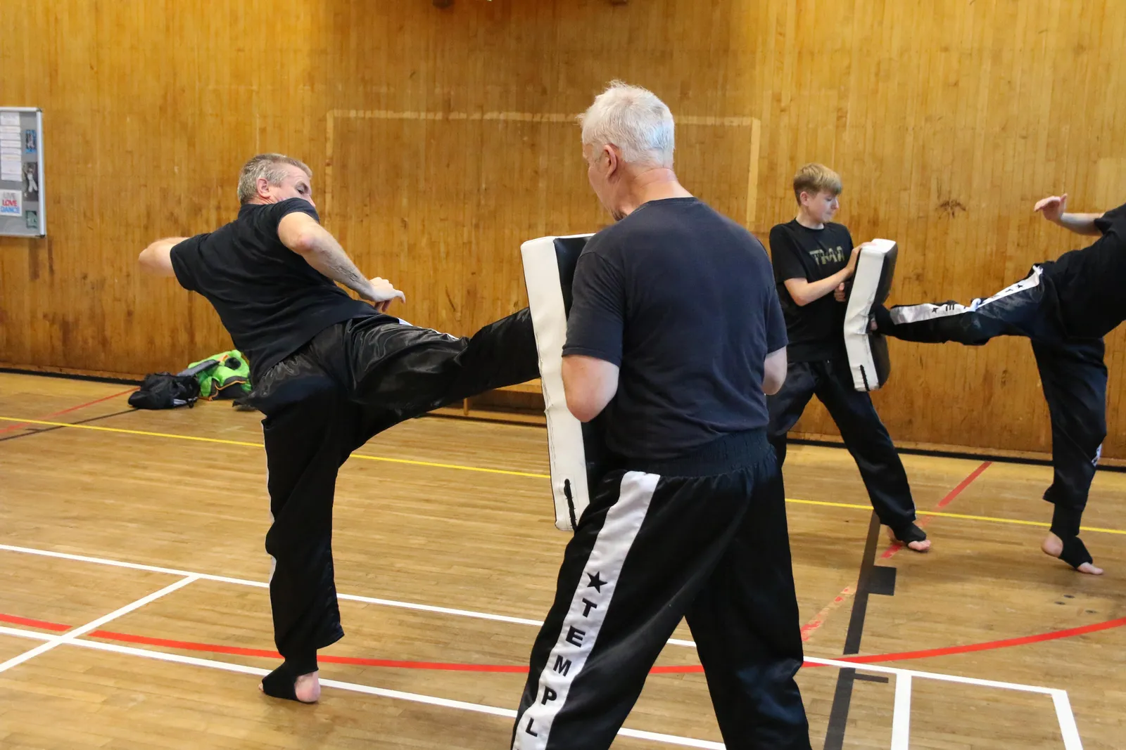 An adult member throwing a high kick into a pad held by his partner